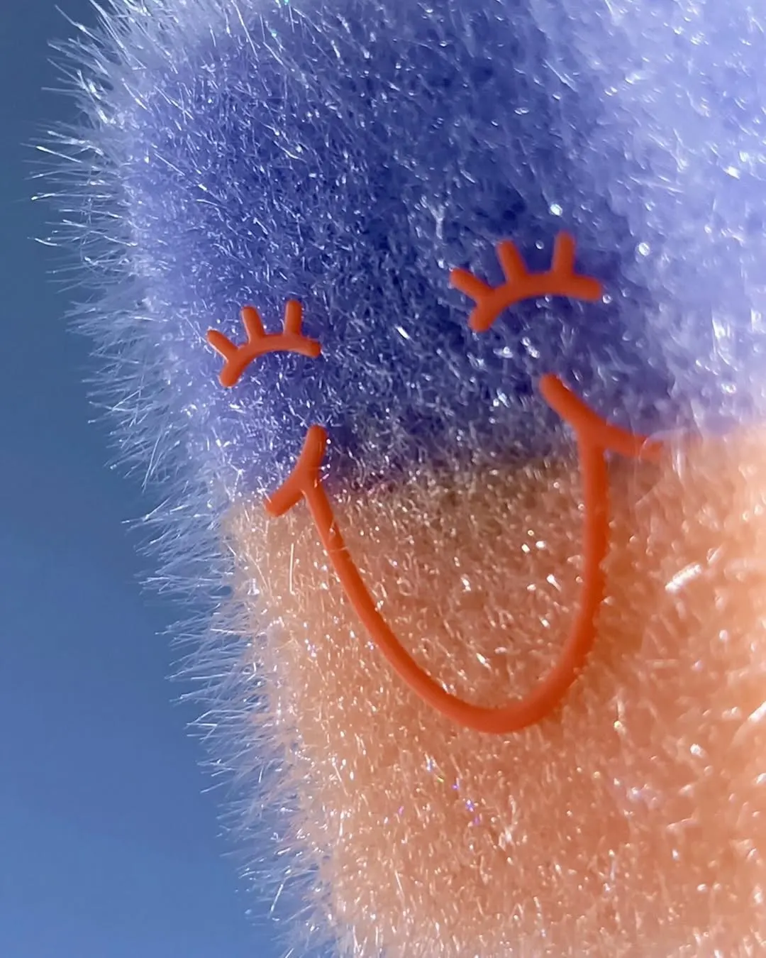 Blue fuzzy sculpture with an orange stitched smile against flowers